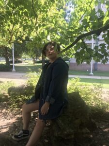 Student posing beneath a tree, sitting on a large rock behind Plaster Student Union. 