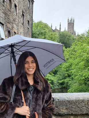 Student poses with umbrella with castle in background