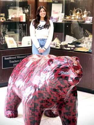 Student poses with bear statue in foreground