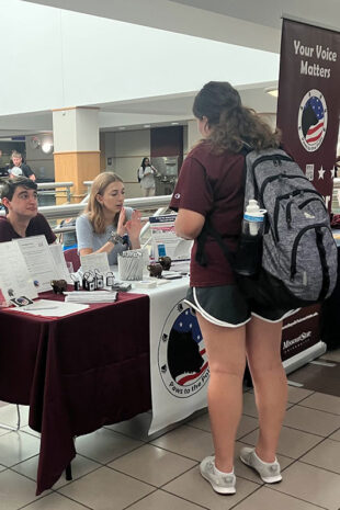 Two individuals at an information table assist a student