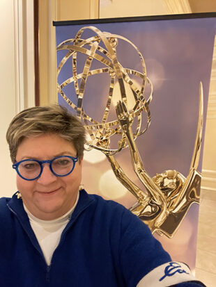 Woman smiling for camera in front of Emmy Award image