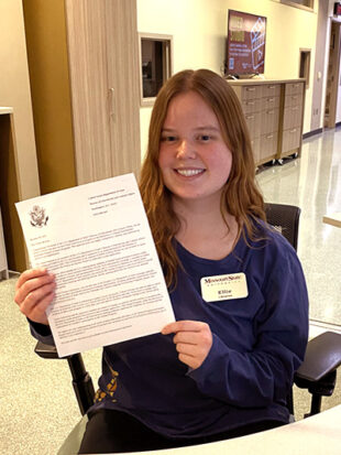 Young woman smiling for camera and showing award letter