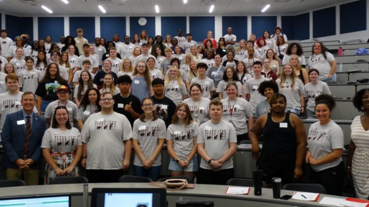 Large group of students pose for a photo in a lecture hall.