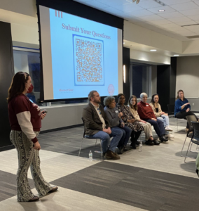 Several people sit in a row in the front of a room.