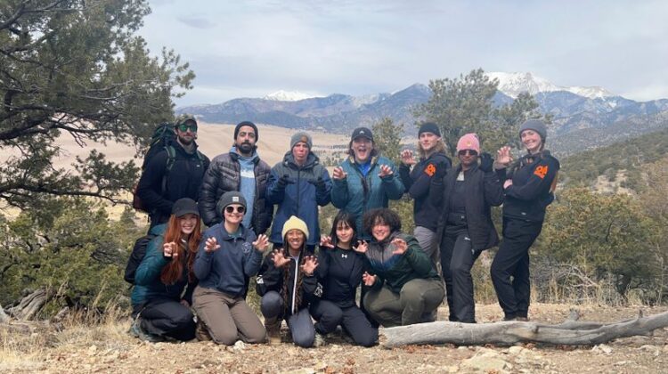 Students hold up bear paws in front of scenic background in Colorado.
