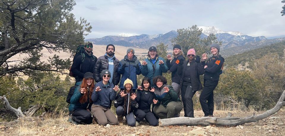 Students hold up bear paws in front of scenic background in Colorado.