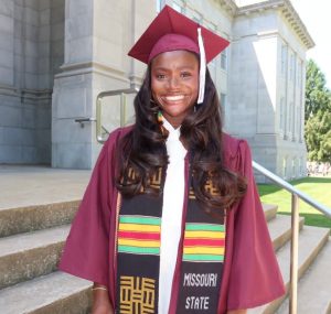 Female student smiles for a photo wearing graduation regalia.