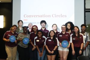 A group of young people in maroon shirts standing in front of a screen displaying "Conversation Circles" and the date September 29.