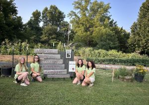 Four students posing in front of a sign that reads "Campus Garden."