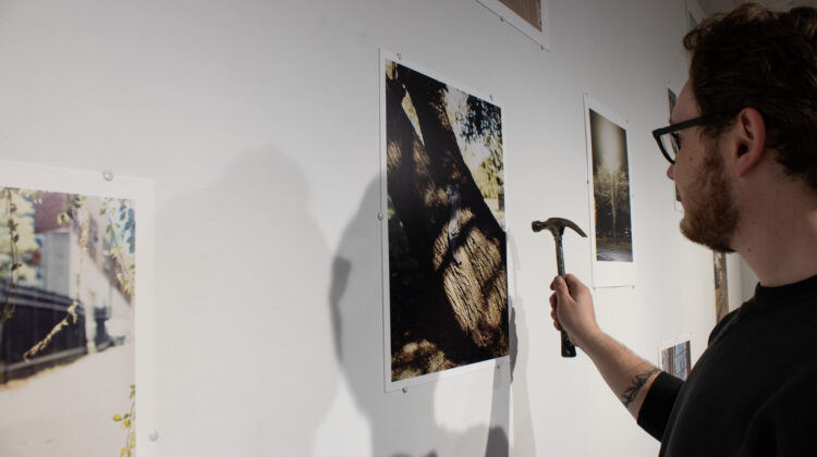 A student using a hammer to hang large photographs on a gallery wall
