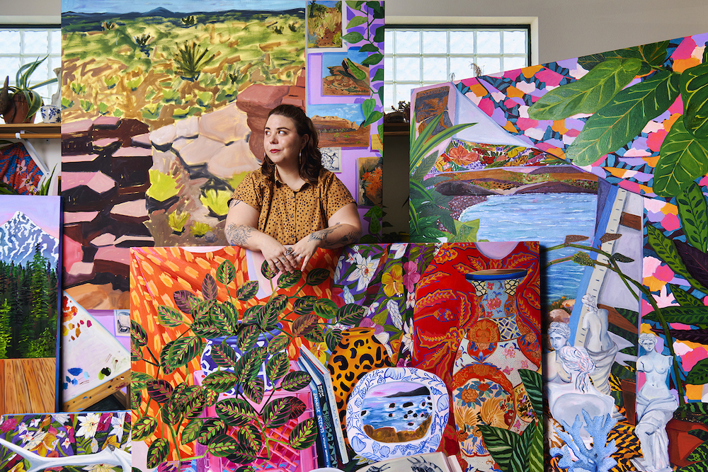 Anna Valdez stands surrounded by large, colorful paintings