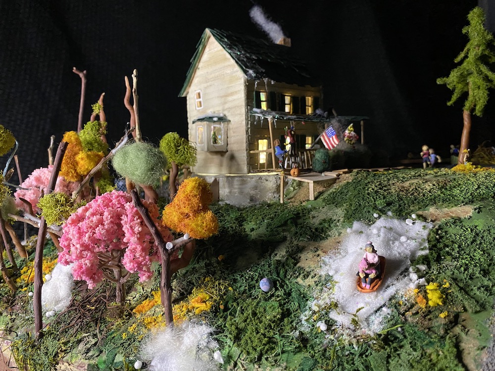 A small model house with whimsical trees and human figures in the yard