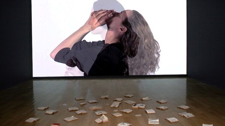 A large screen projecting overlapping side profiles of two women, with open books on the floor below the screen