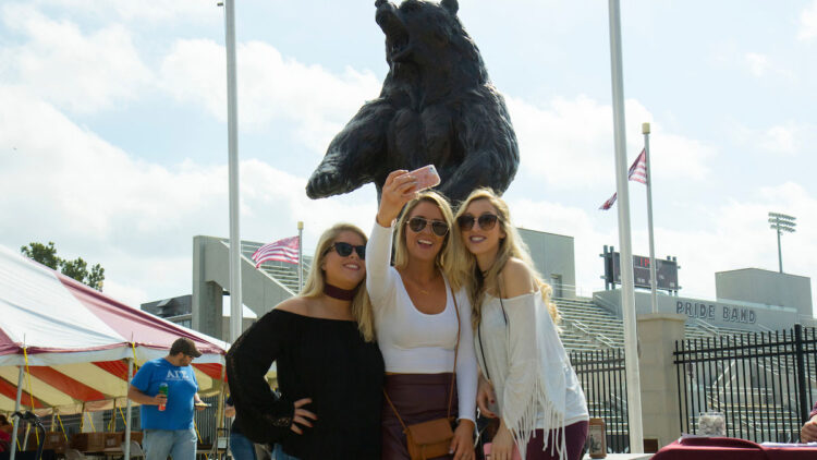 students taking a selfie with bear statue