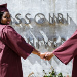 Alumni in graduation gowns in front of Missouri State sign