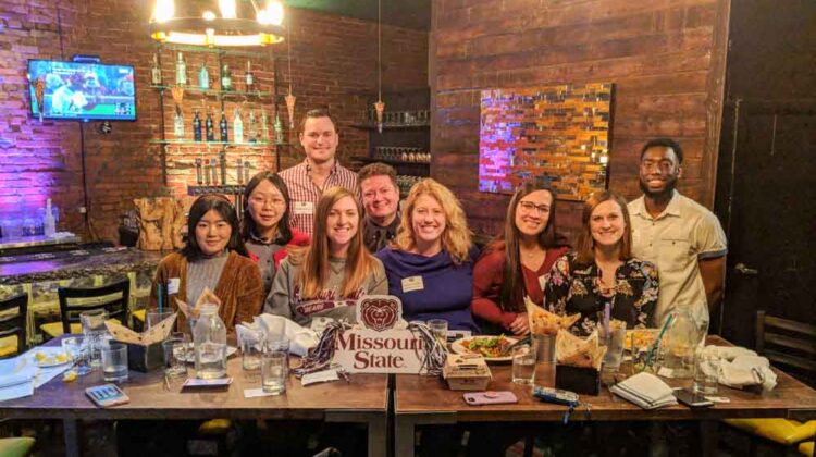 ten people standing at a table smiling