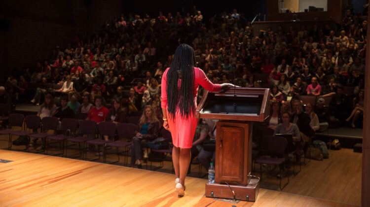 woman stands on stage in front of crowd