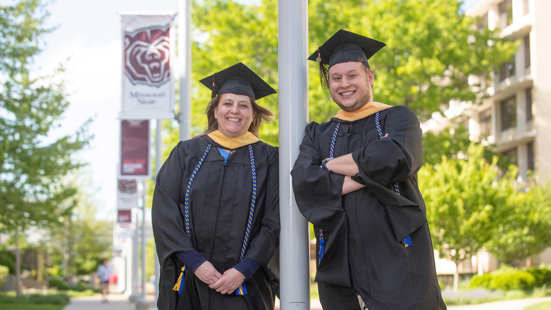 Jayma and Ethan Porter standing in their graduation gowns on campus