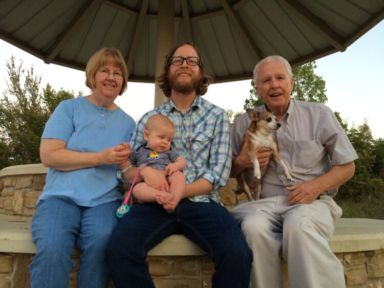 Three people pose with a baby and a dog