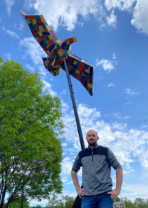 Jeff Moore standing next to a large-scale sculpture of a multi-colored eagle 
