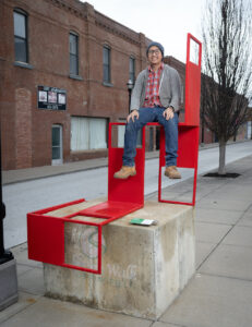 Artist Timothy Damaso sitting on a large red sculpture in Downtown Springfield