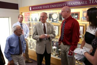 Dr. Tommy Burnett (right) and Missouri State President Clif Smart stand in front of the handball team’s trophy case, circa 2014.