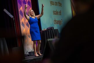 Kim Becking speaks on stage at an event.