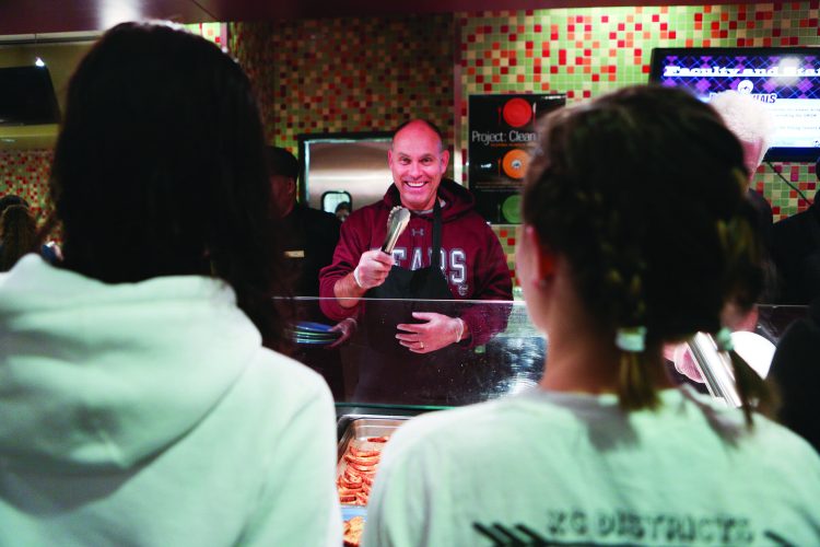 Image of Brent Dunn smiling while serving food to two students