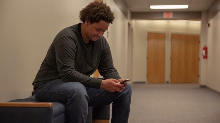 Michael sits on a bench in a hallway looking at his phone