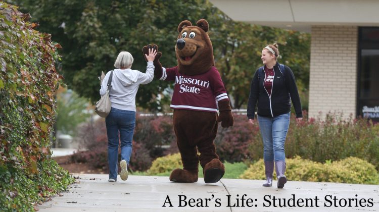 Boomer Bear is giving a student a high five on campus.