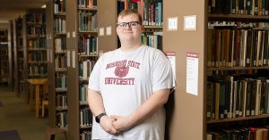Daniel Paige poses professionally next to a bookcase in the library.