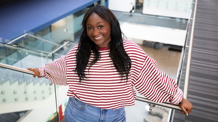 Portrait of Kamryn Middleton, a finance and entrepreneurship major, posing next to a stairwell in Glass Hall.