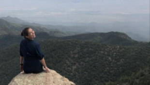 Krissy Sardina sits on a rock surrounded by mountains. Photo courtesy of the Oklahoma Fish and Wildlife Conservation Office newsletter.