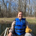 Daphne Miles on a small boat smiling wearing a blue life vest giving a thumbs up