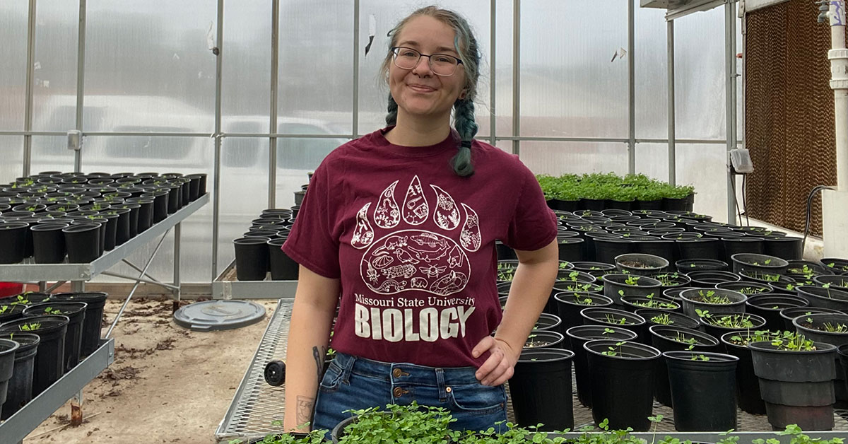 Abilene Mosher grins as she works with growing plants in a greenhouse.