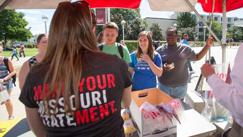 A staff member wearing a Make Your Missouri Statement T-shirt hands out swag to students
