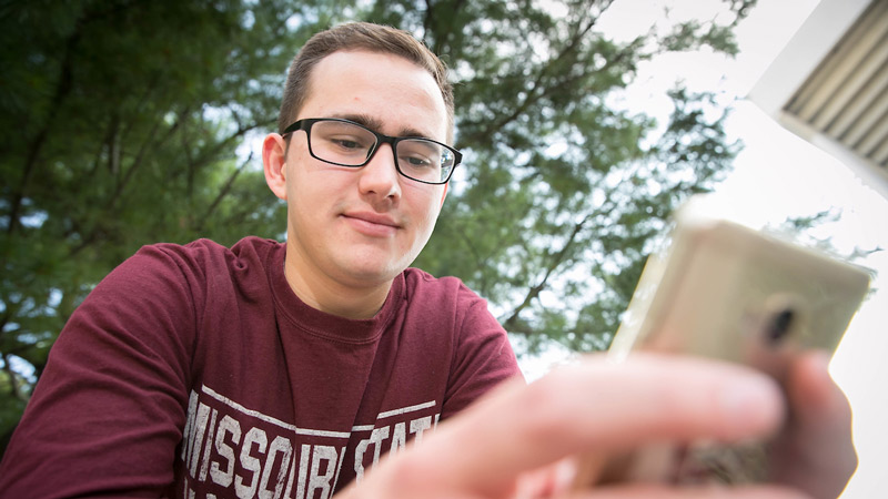 A male student in a maroon shirt uses his iPhone.