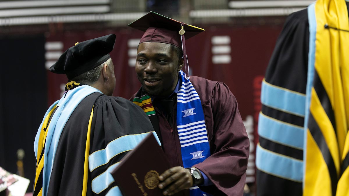 A graduate shakes hands with a faculty member at commencement.
