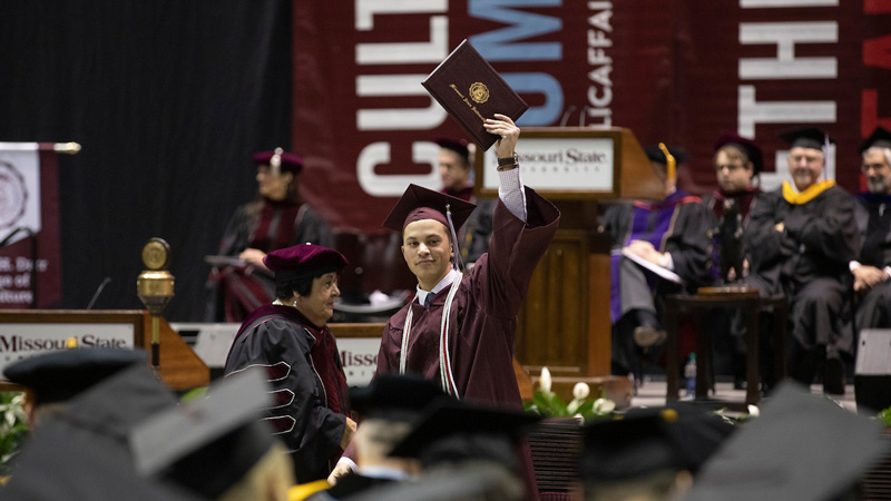 A graduate proudly holds up his maroon diploma cover.
