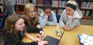 Children gather round a computer as they learn science through robotics