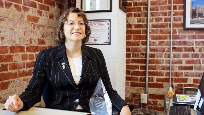 Dr. Follensbee sits at her office desk behind her service-learning award