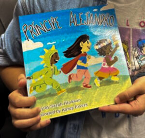 Sarah holds the book, showing the front cover of illustrations of children in costumes running and smiling