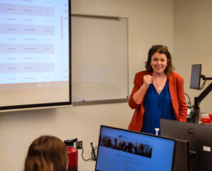 A woman in a classroom smiles at a group of students - showing Lori Rogers and her interaction with students