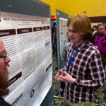 A young man smiles as he stands next to a display of his research