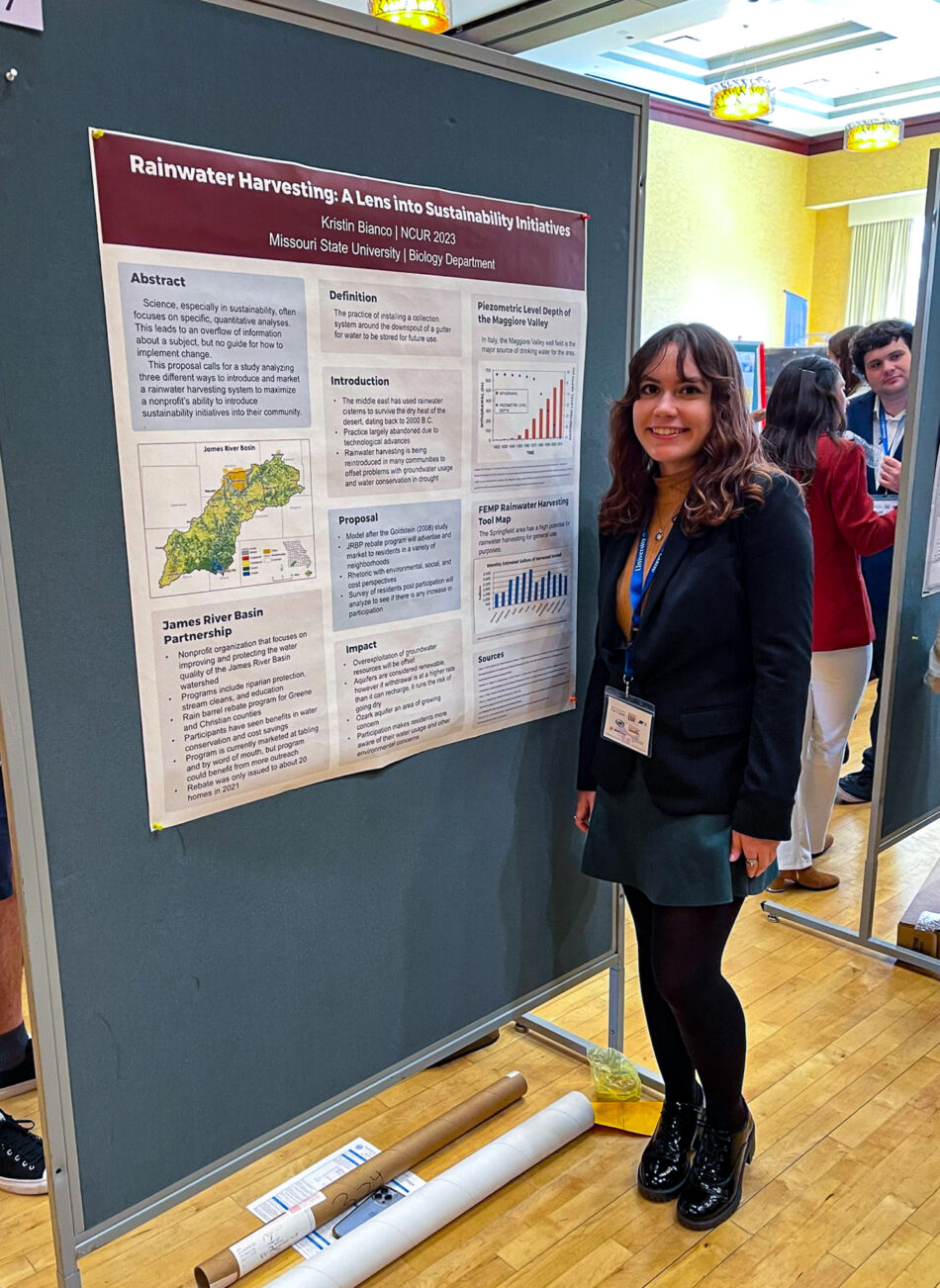 A young woman smiles and poses next to a display of her research
