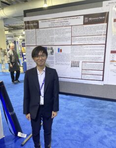 Joe Truong stands in front of his presentation board at a science conference.
