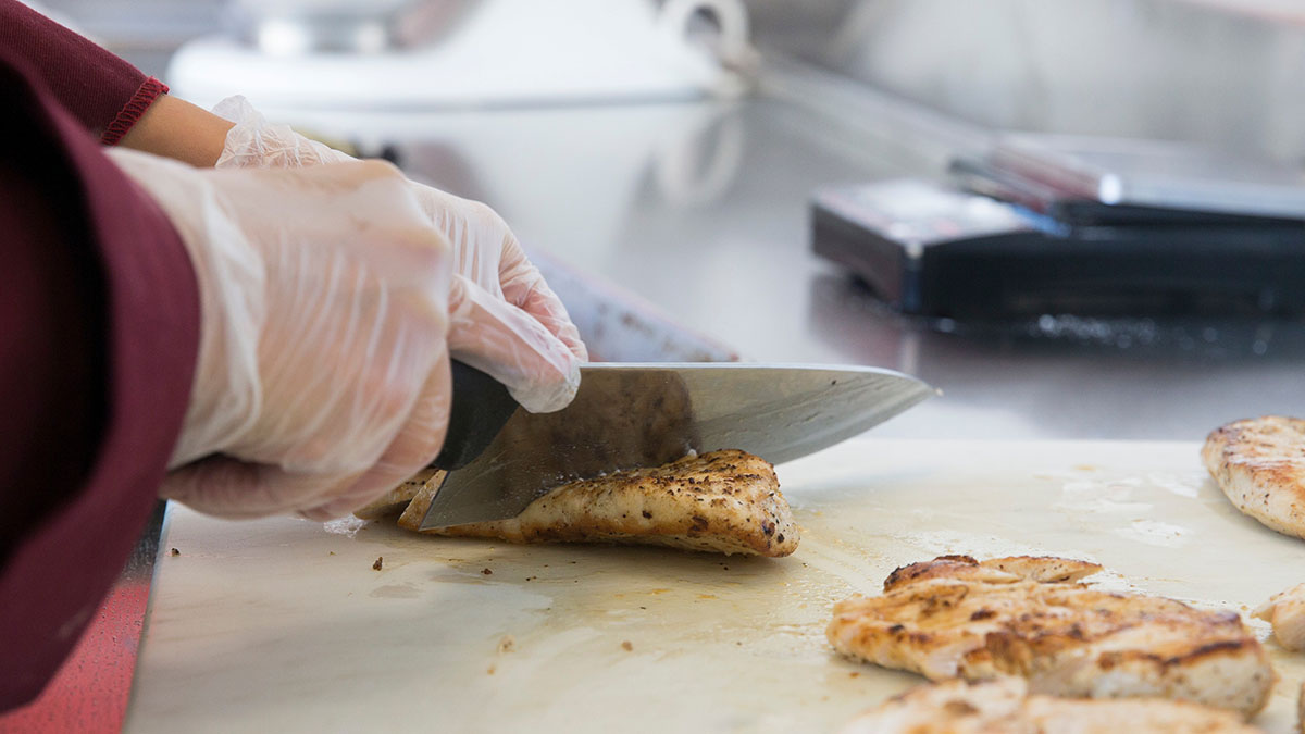 Chef slices chicken while wearing sanitary gloves.