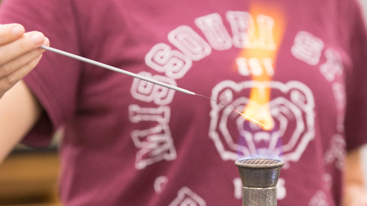 A female student in a Missouri State University T-shirt operates a burner.