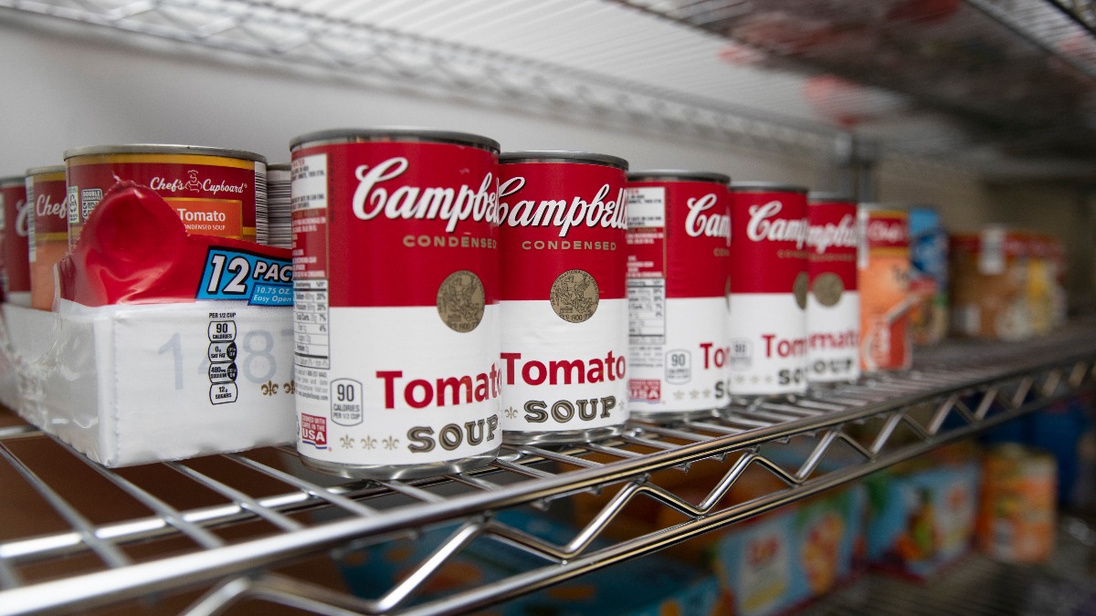 A row of soup cans rests on a storage shelf.