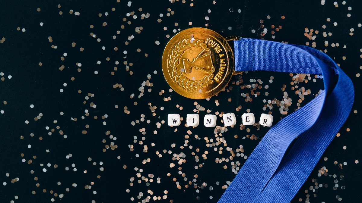 A medal labeled "winner" surrounded by dice that spell the same word. Photo by Nataliya Vaitkevich from Pexels.